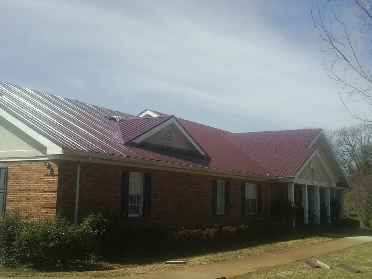 Red metal roof with gabled entries on a long brick building, from a Hail Damage Roof Repair job in Ford