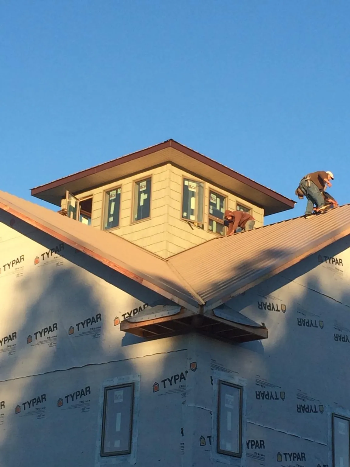 Roofers working around a rooftop cupola on a new metal roof at sunset in Ford